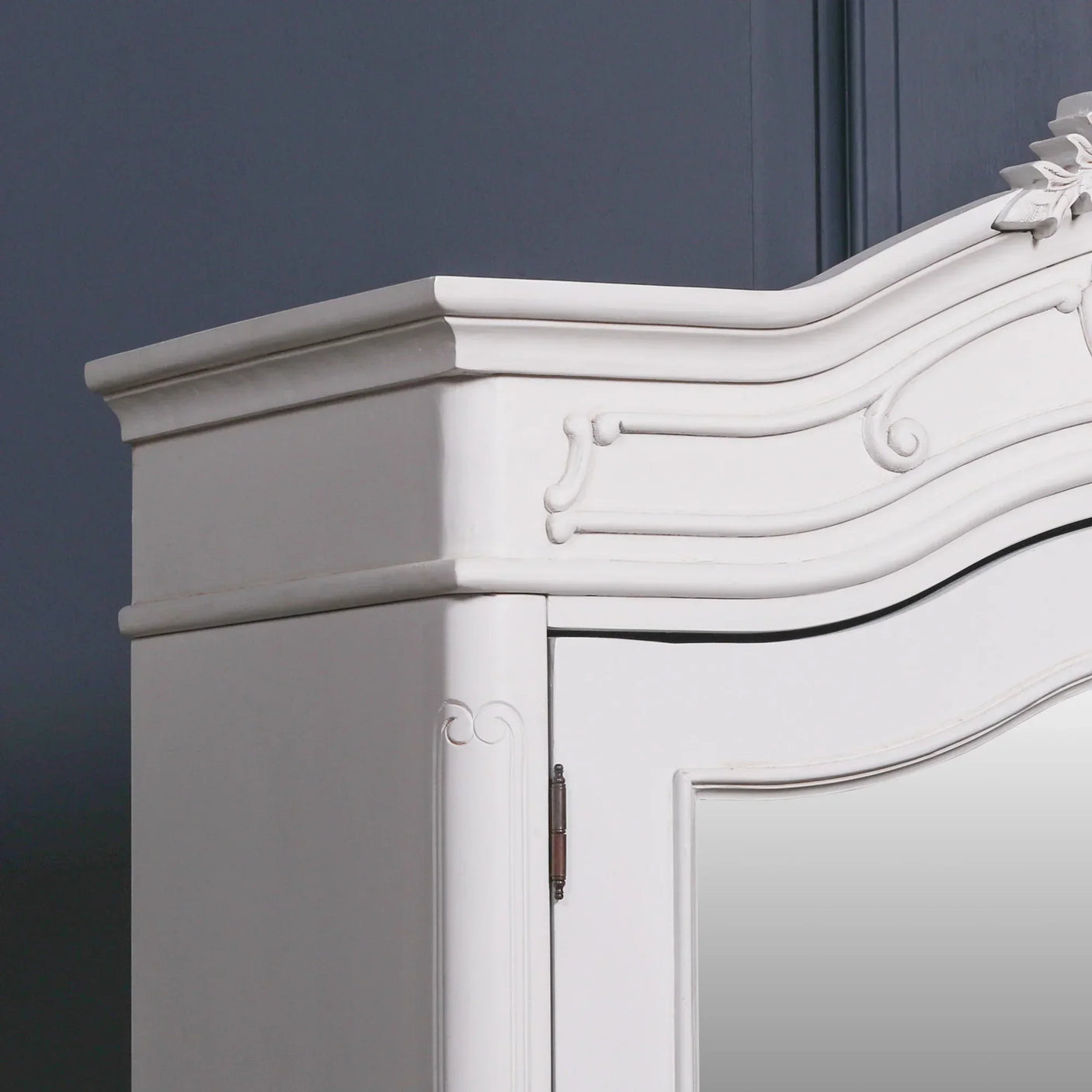 White wooden wardrobe with ornate trim and curved detailing, close view of upper corner