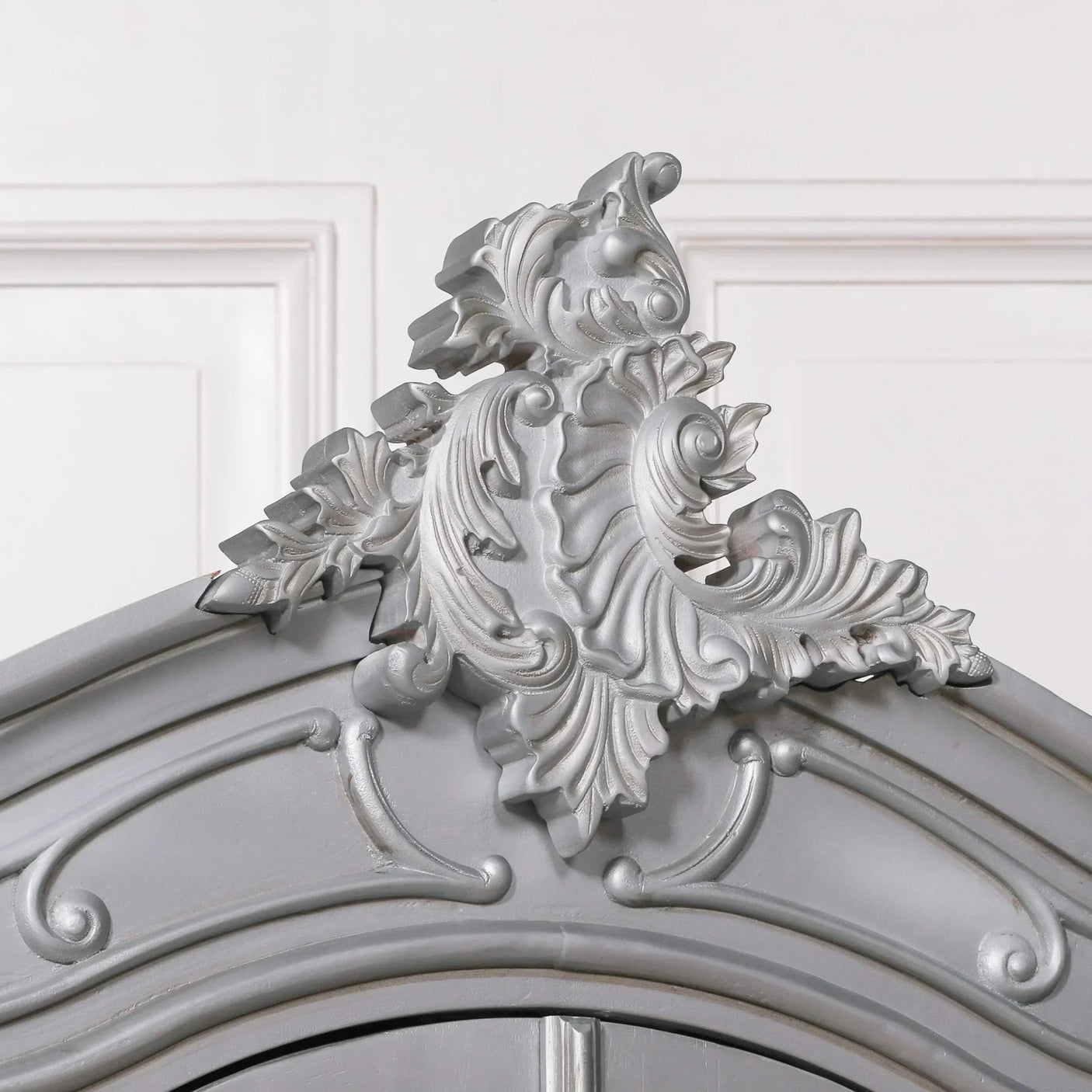 silver wardrobe top with ornate carved detailing against a white wall