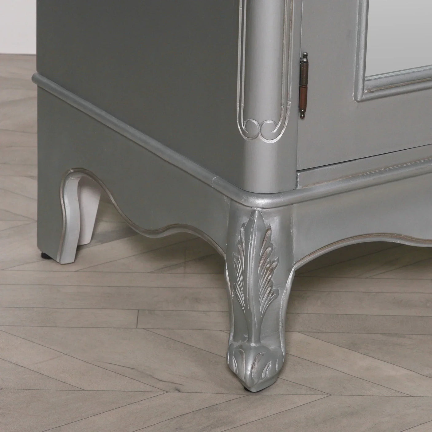 Silver painted wood cabinet leg with carved detail on light herringbone floor