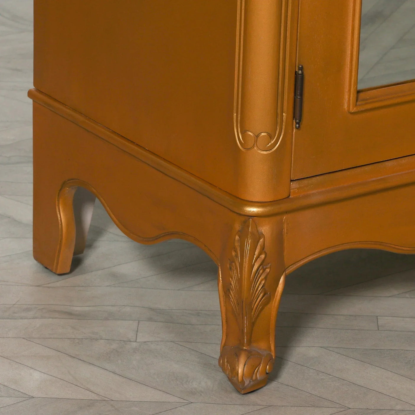 Close-up of wooden cabinet leg with carved leaf detail and gold finish on tiled floor
