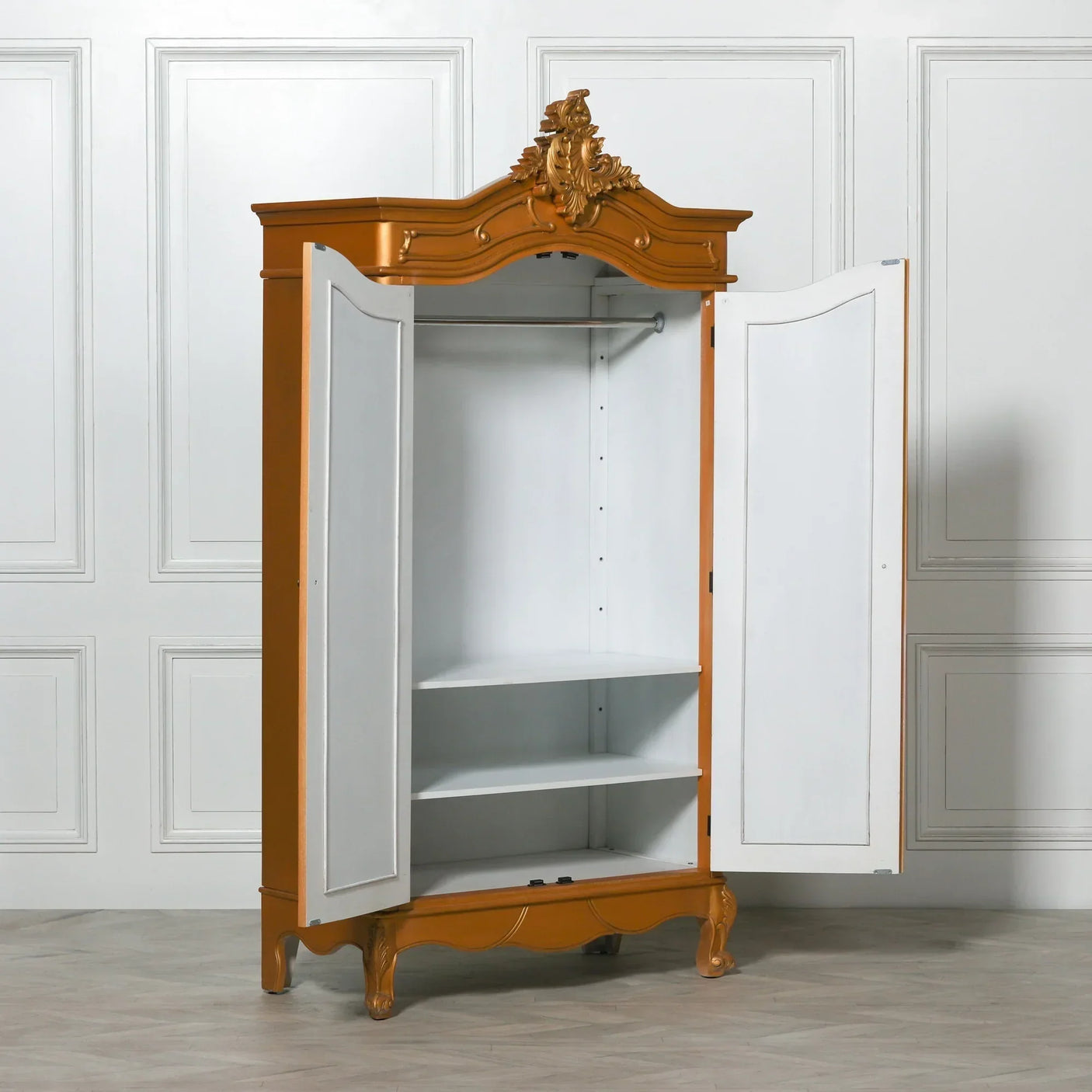 Ornate gold wardrobe with open doors, interior shelves and hanging rail, against white wall
