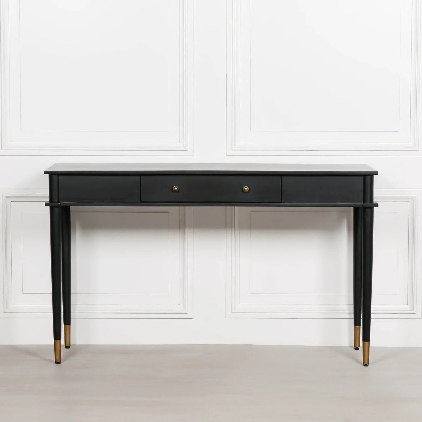 Black console table with two drawers and gold-tipped tapered legs against white wall