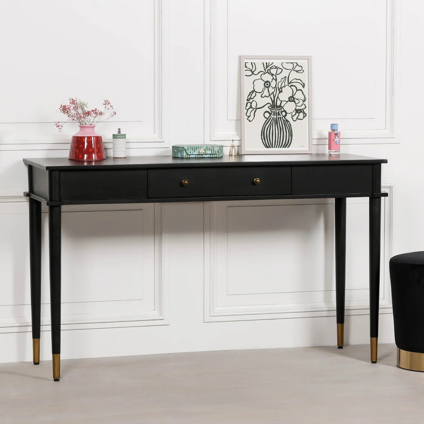 Black console table with gold-tipped legs, two drawers, and decorative items on top