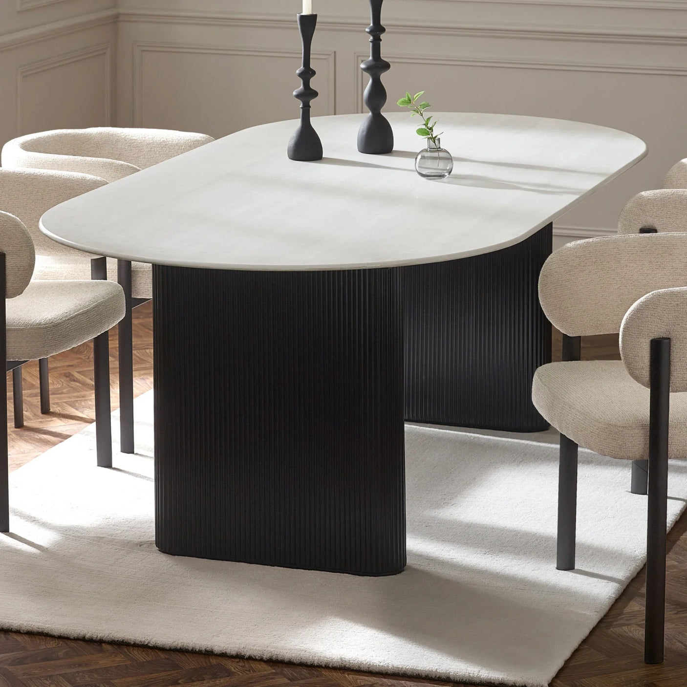 Rectangular dining table with white top and black fluted base, surrounded by cream chairs