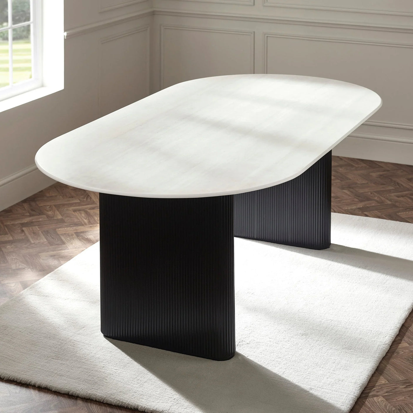 Modern dining table with oval white top and black ribbed pedestal legs on cream rug