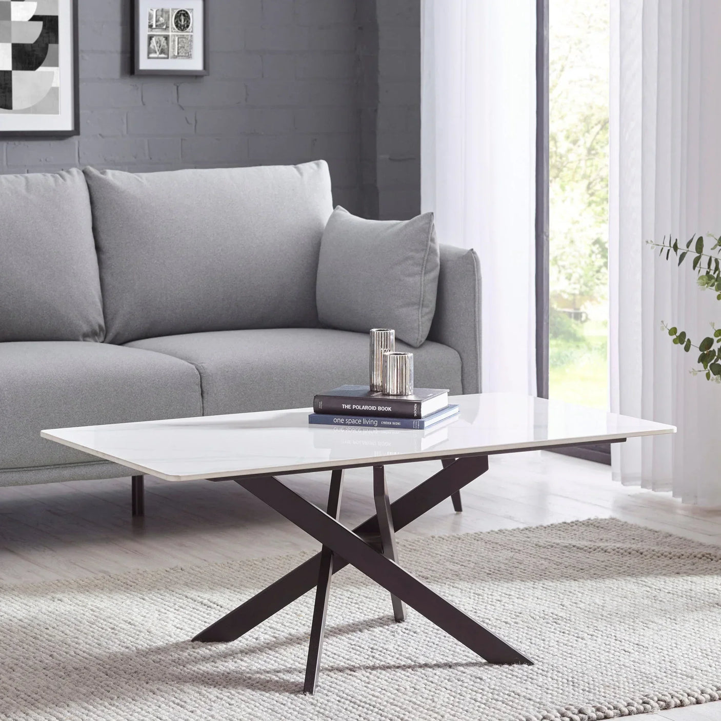 White marble coffee table with black crossed legs in modern living room next to grey sofa