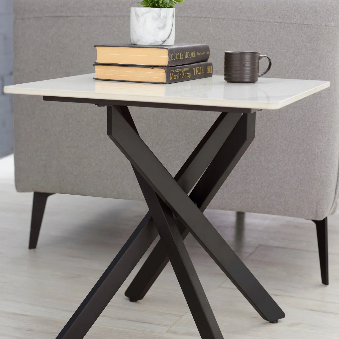 White marble lamp table with black metal legs beside grey sofa, books and mug on top