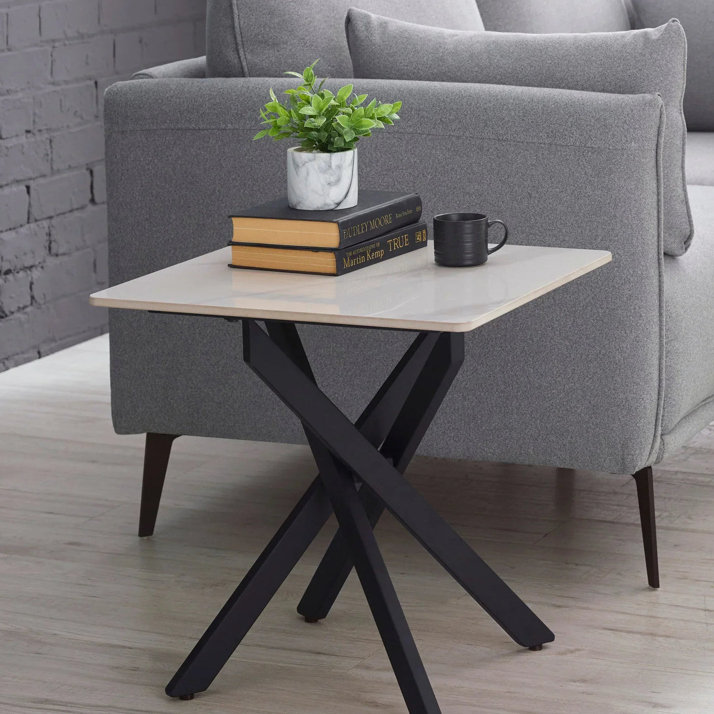 White marble lamp table with black metal legs beside grey sofa, books and plant on top
