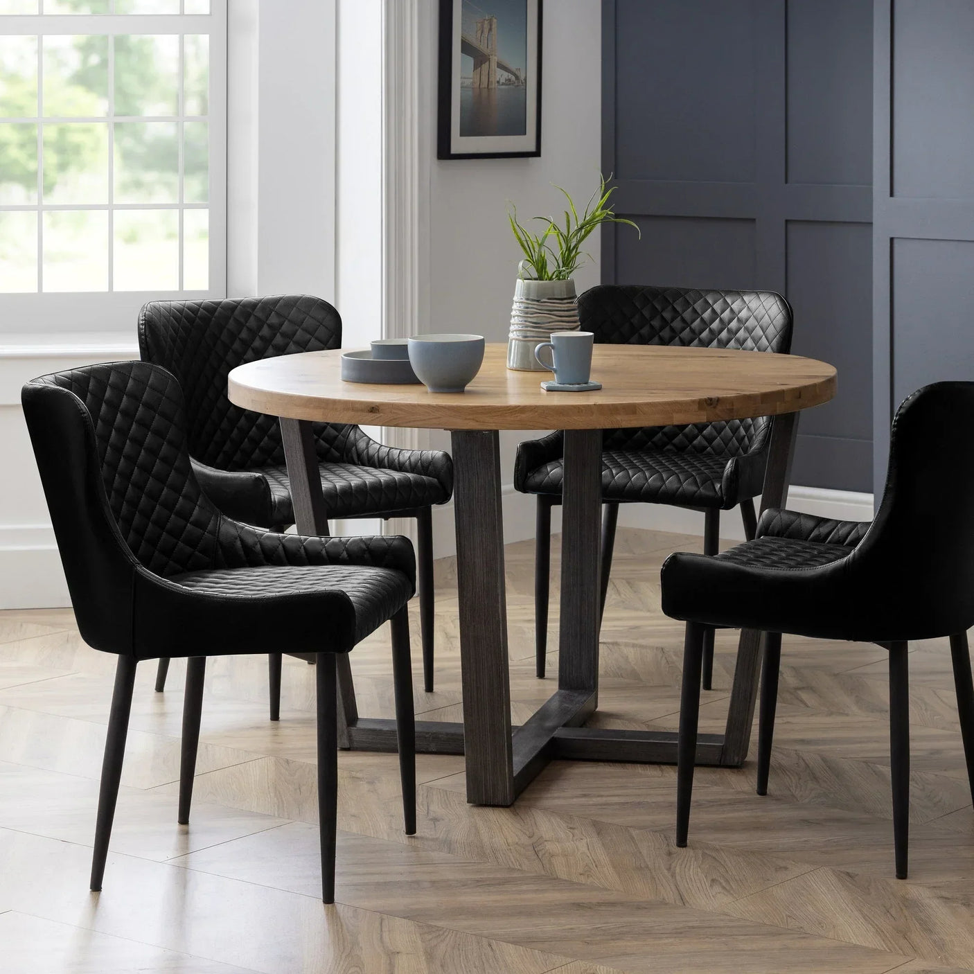 Round oak dining table with black quilted chairs in modern dining room