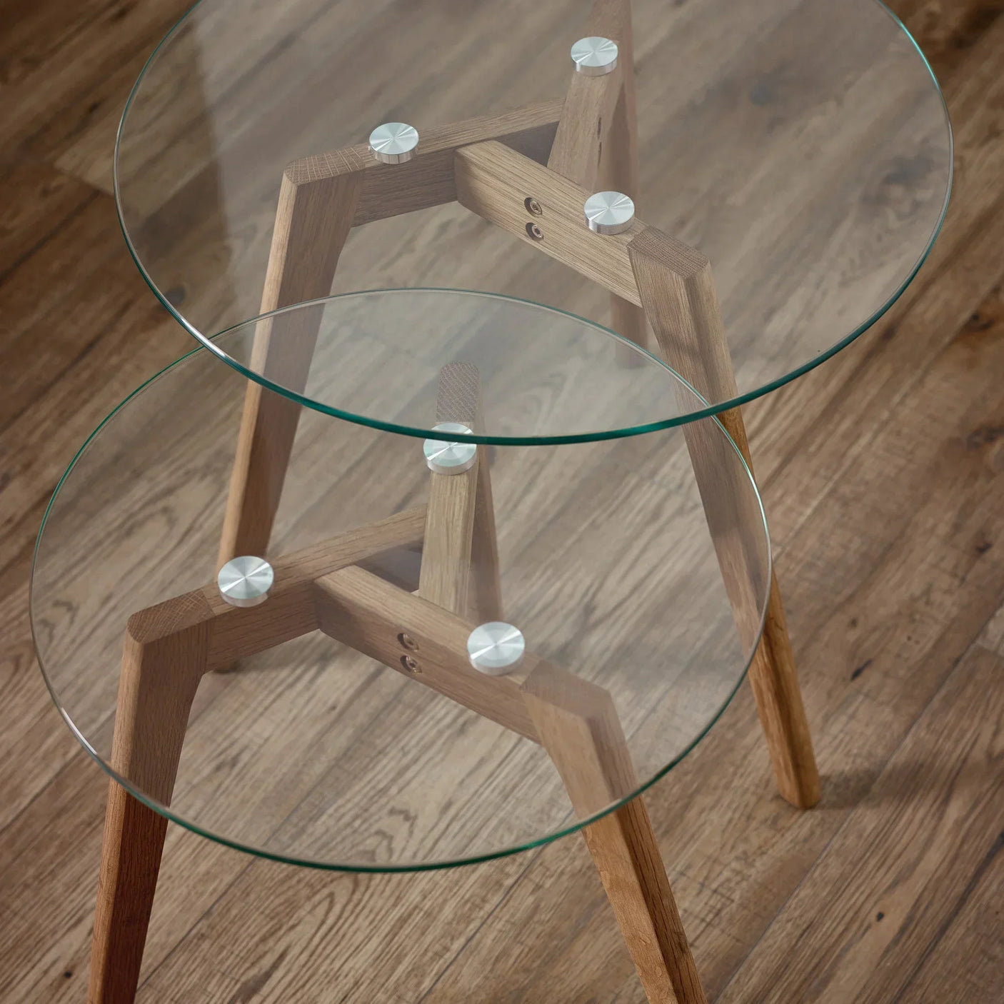Round glass nest of tables with light wood frames on wooden floor, close-up detail