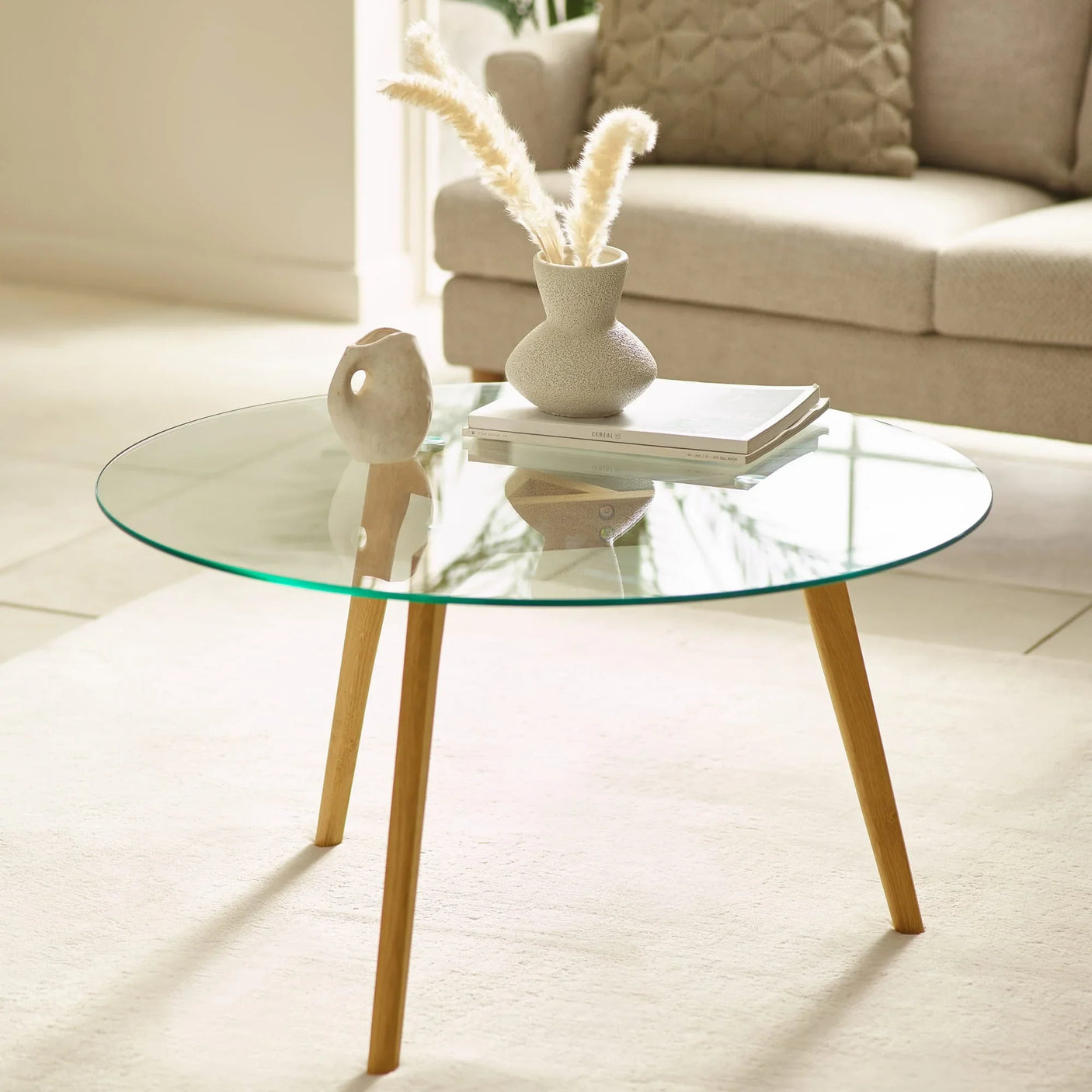 Round glass coffee table with wooden legs styled with books and vase in modern living room