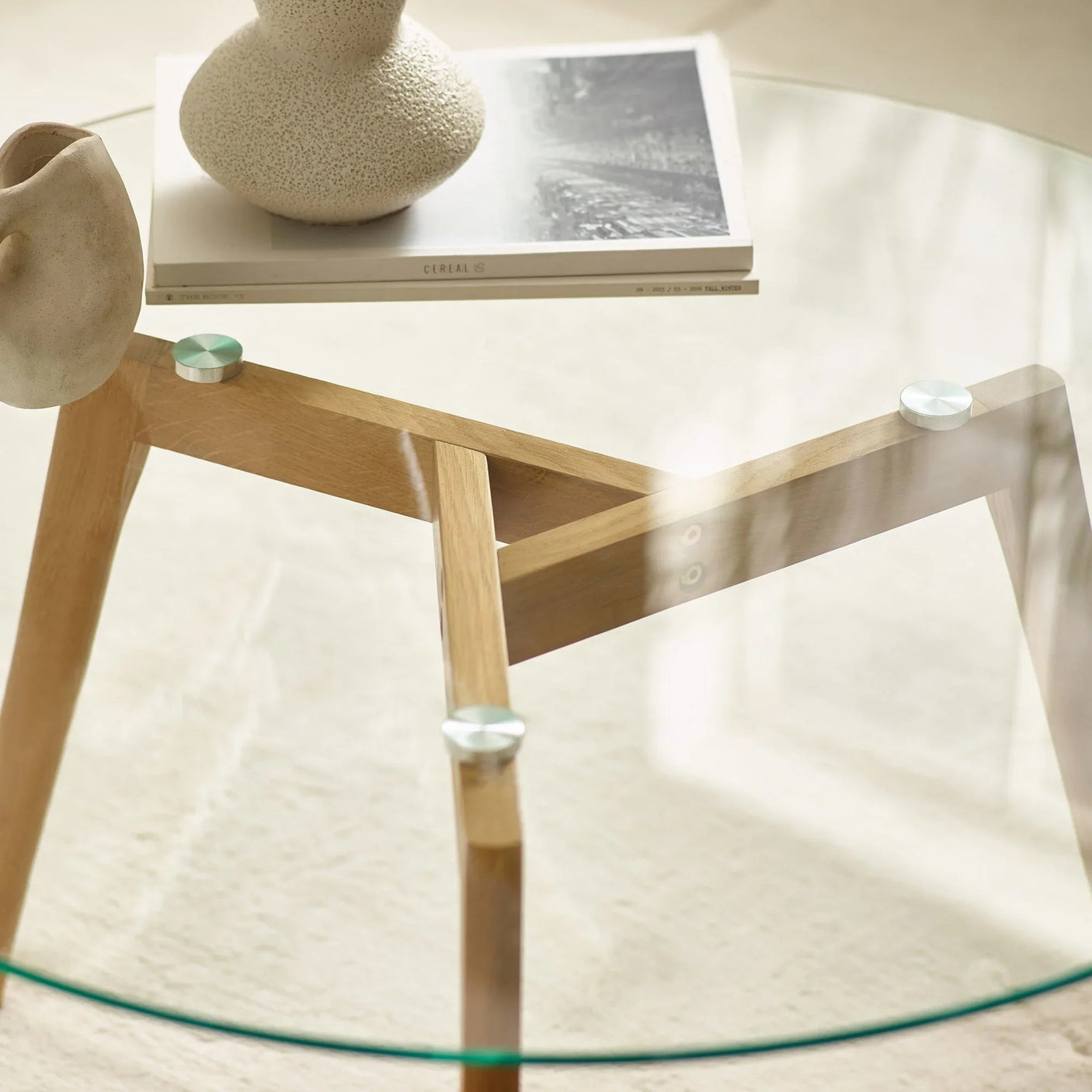 Round glass coffee table with wooden legs, decorative vases, and magazine on top