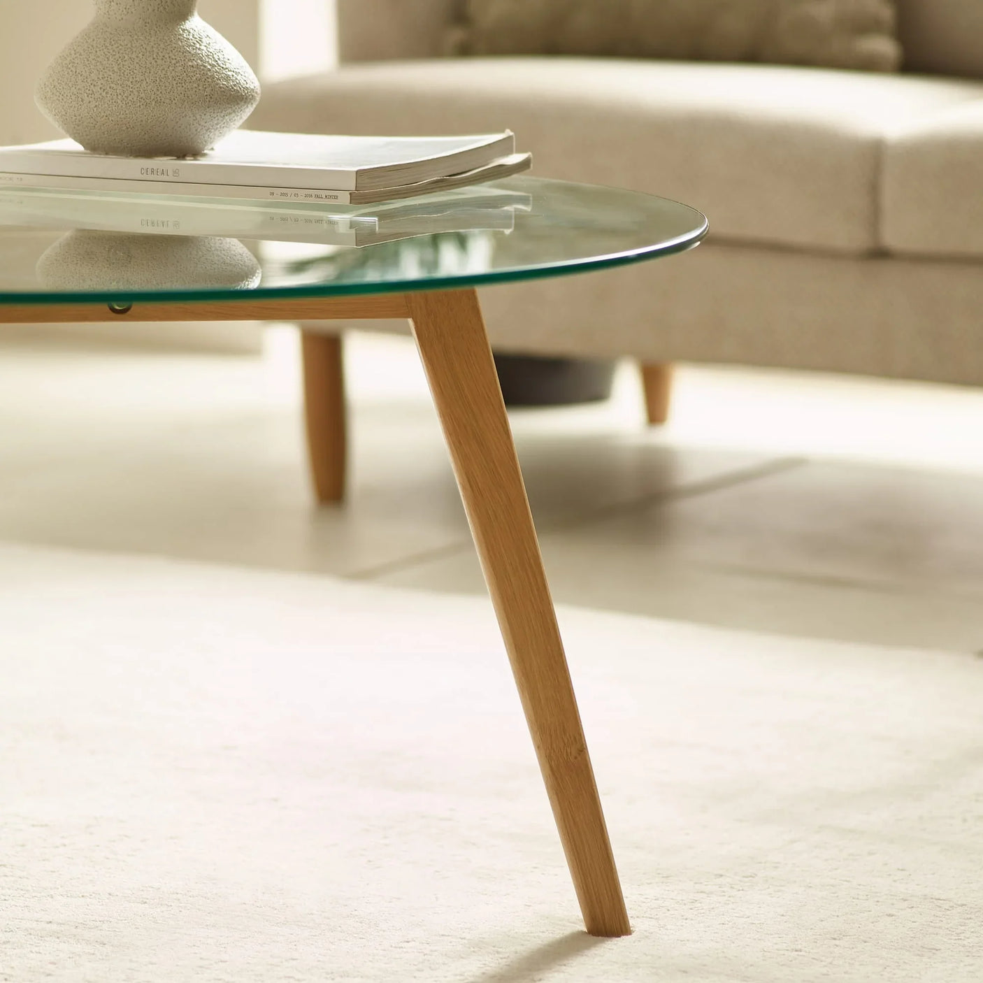 Glass coffee table with wooden legs in living room, books and vase on tabletop