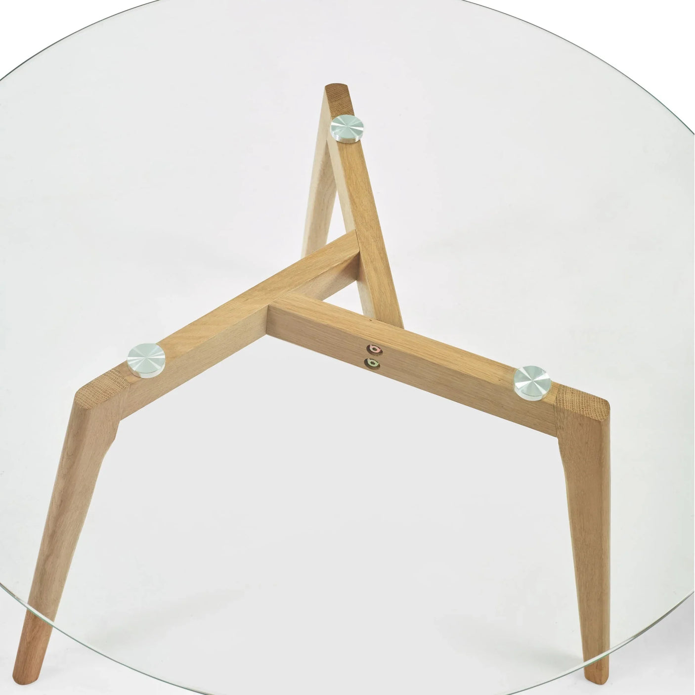 Round glass dining table with light wood tri-leg base and metal fixings
