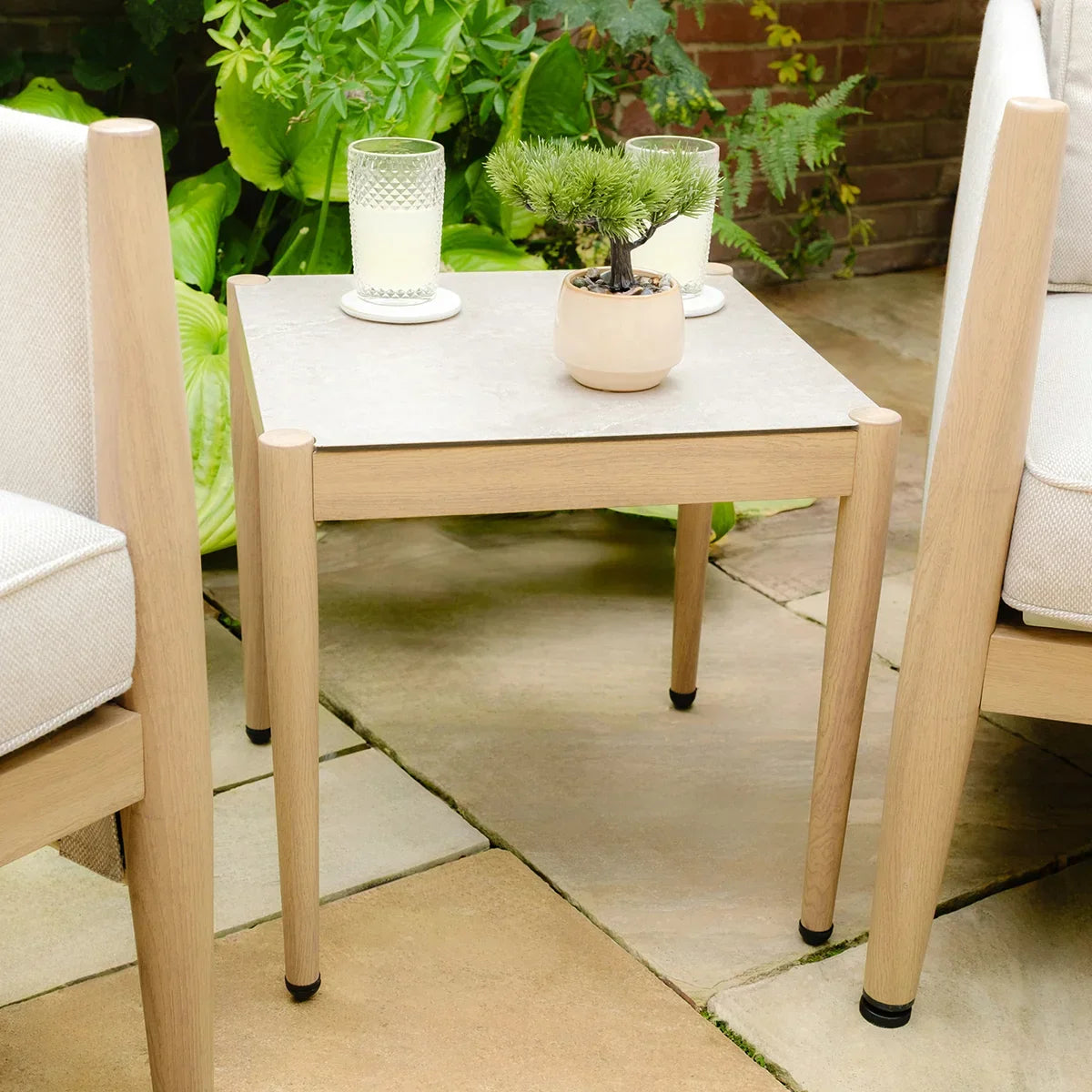 Outdoor wooden side table with light stone top, two drinks and a small plant, patio setting