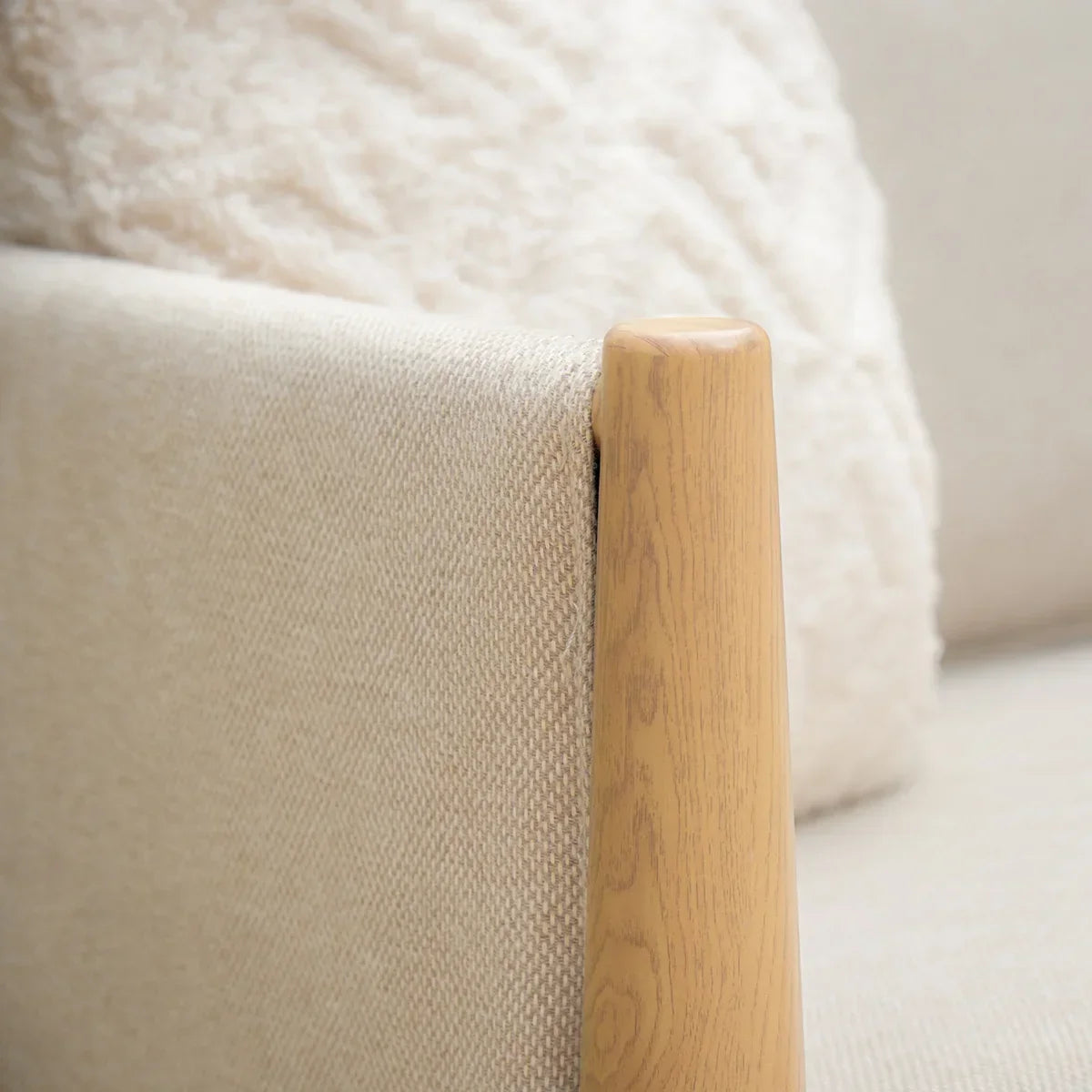 Beige fabric sofa armrest with light wood detail and soft textured cushion