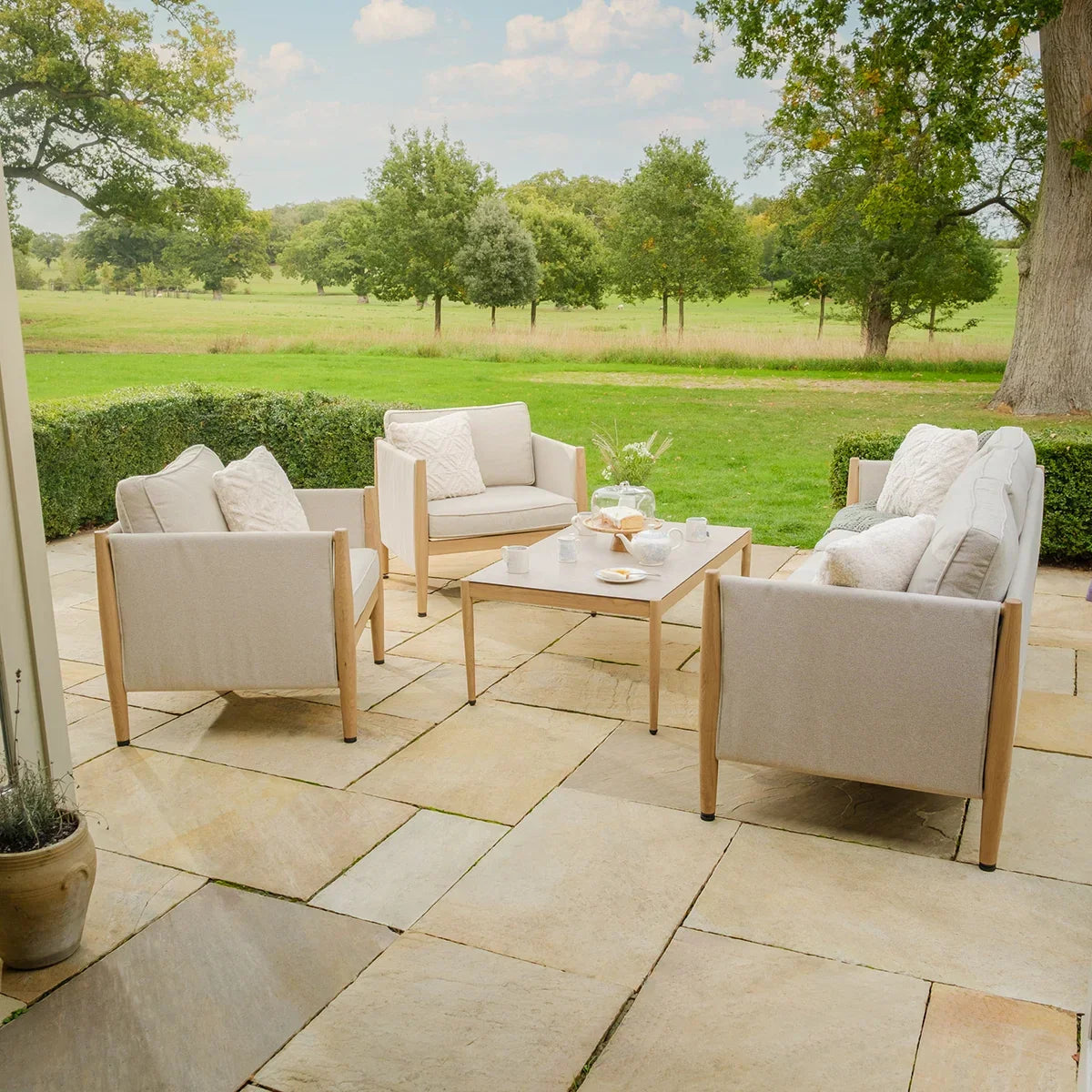 Beige outdoor lounge furniture set with wooden frames on stone patio, garden view