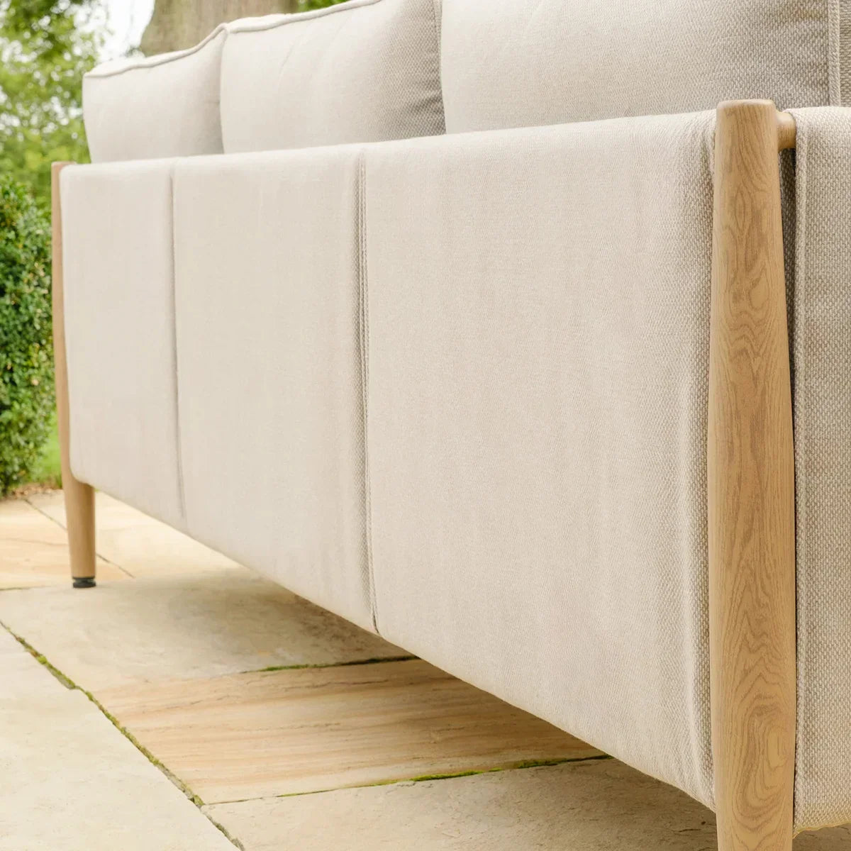 Beige fabric outdoor sofa with wood legs viewed from the back on a patio