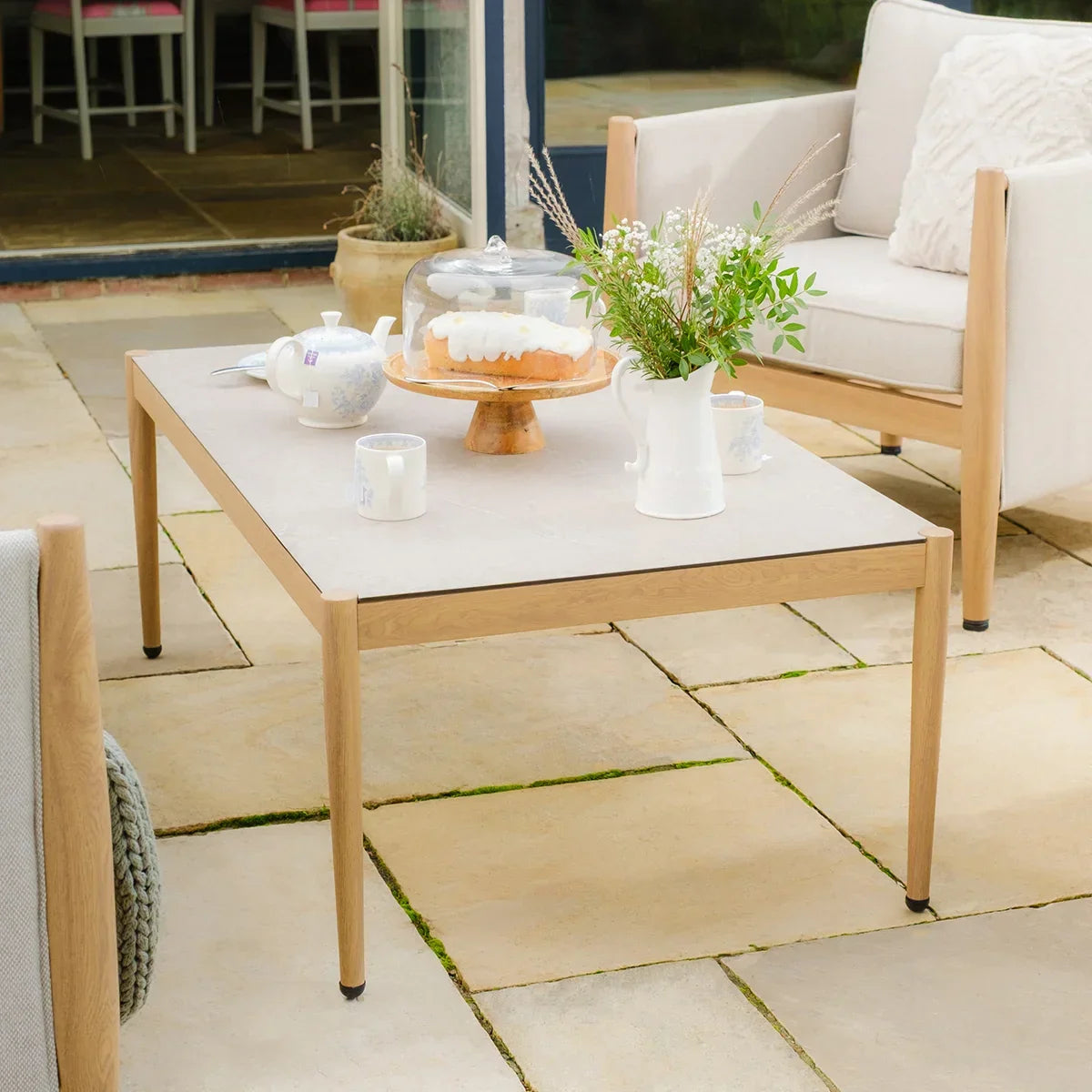 Outdoor coffee table with light wood frame on patio, styled with cake, teapot and flowers