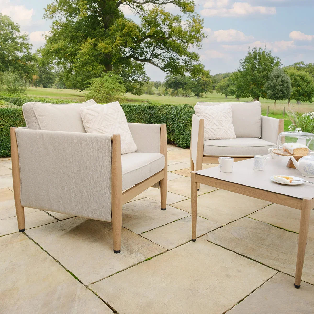 Beige outdoor sofa set with wooden frames and coffee table on patio, countryside backdrop