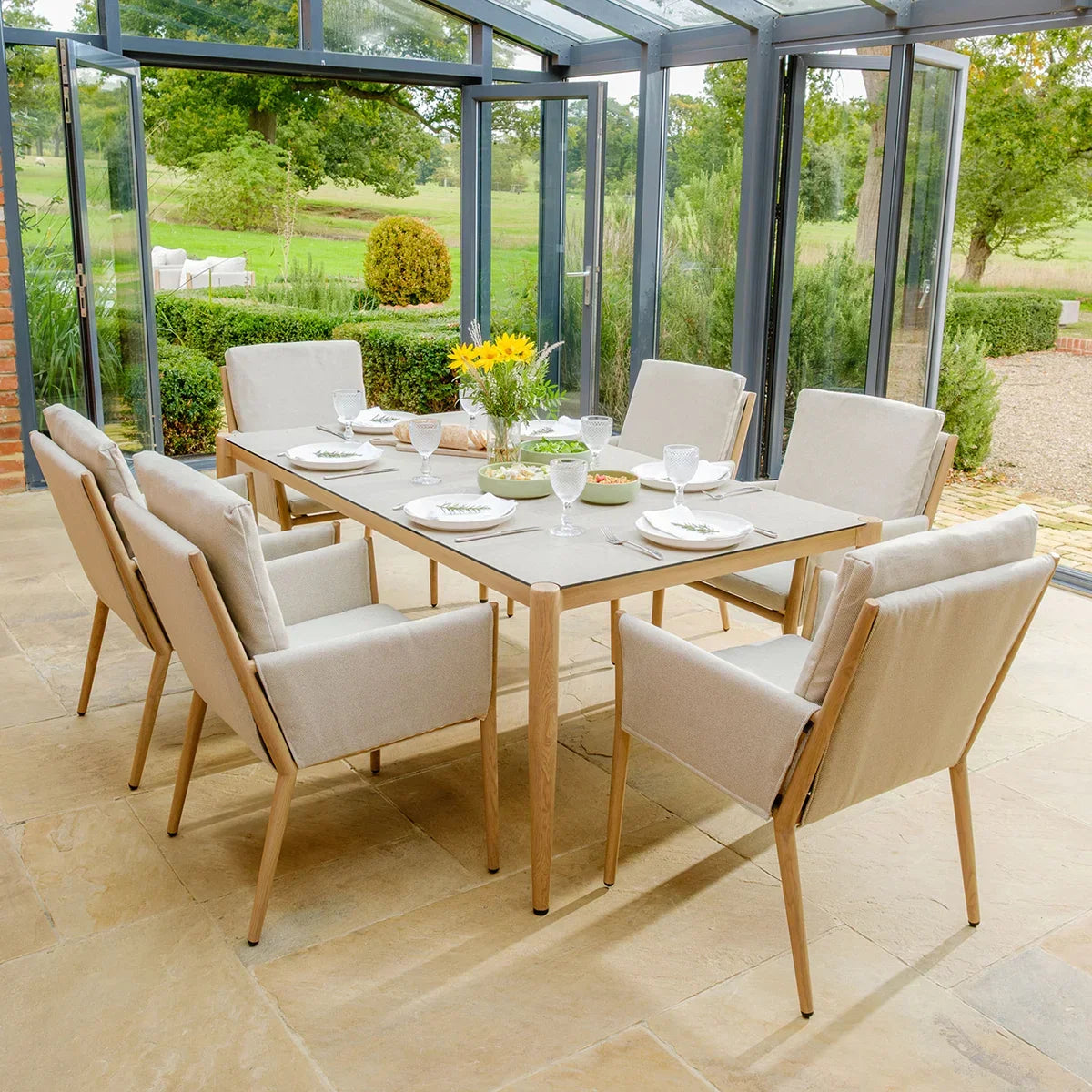 Beige garden dining set with six cushioned chairs and table in bright conservatory