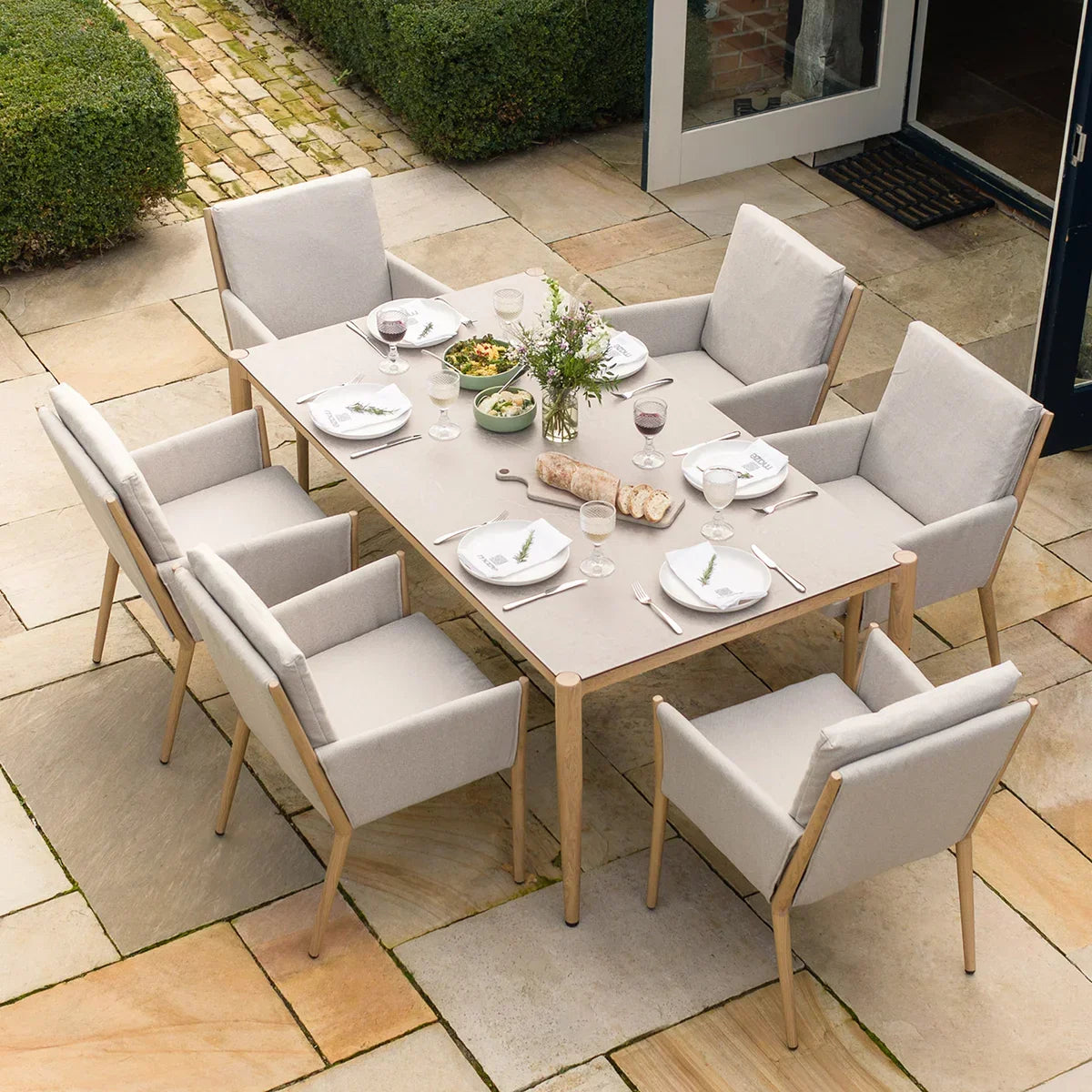 Rectangular outdoor dining table set with eight cushioned armchairs on stone patio