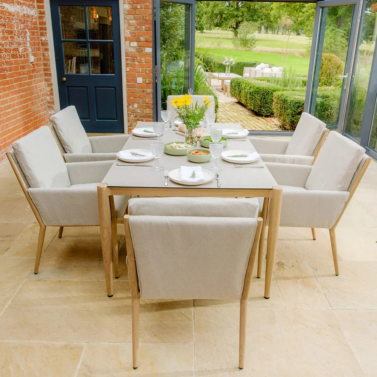 Six seat beige dining set with padded armchairs in glass conservatory, table set for meal