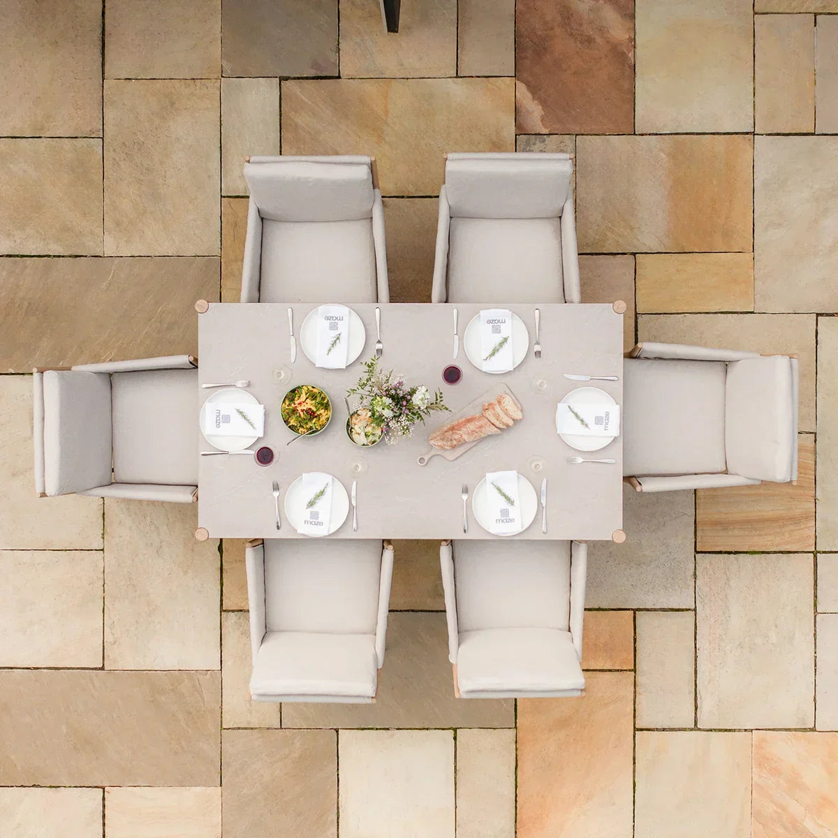 Rectangular outdoor dining table with six beige cushioned chairs on stone patio