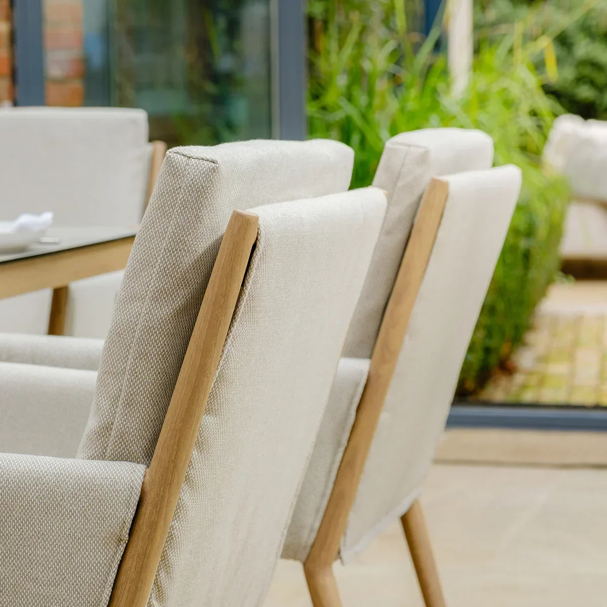 Beige upholstered dining chairs with wooden frames beside outdoor dining table