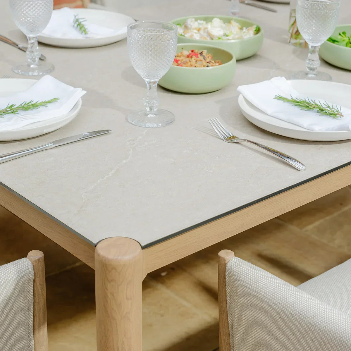 Rectangular beige ceramic dining table with wood frame, set with plates and glassware
