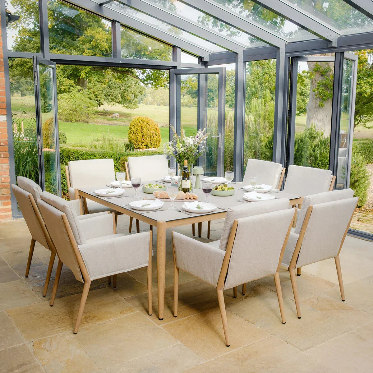 Eight seater beige dining set with padded chairs and rectangular table in a glass conservatory