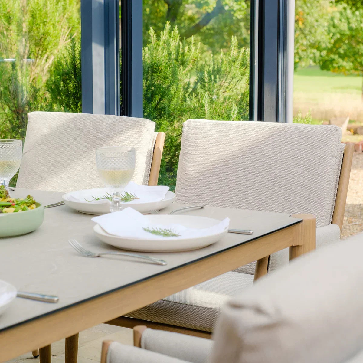 Beige cushioned dining chairs and wooden table set for outdoor dining by large windows
