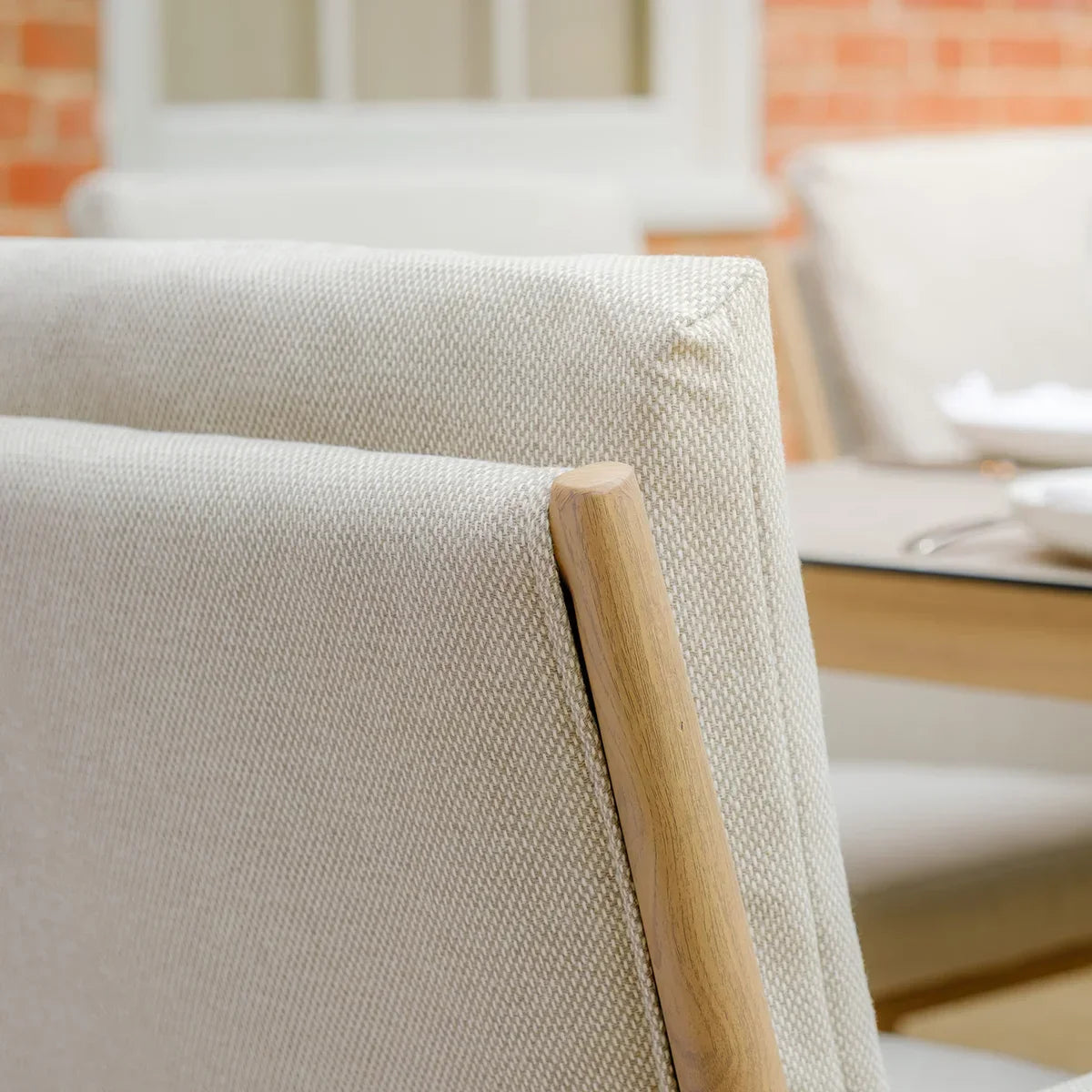 Close up of beige outdoor dining chair with light wood frame and textured fabric