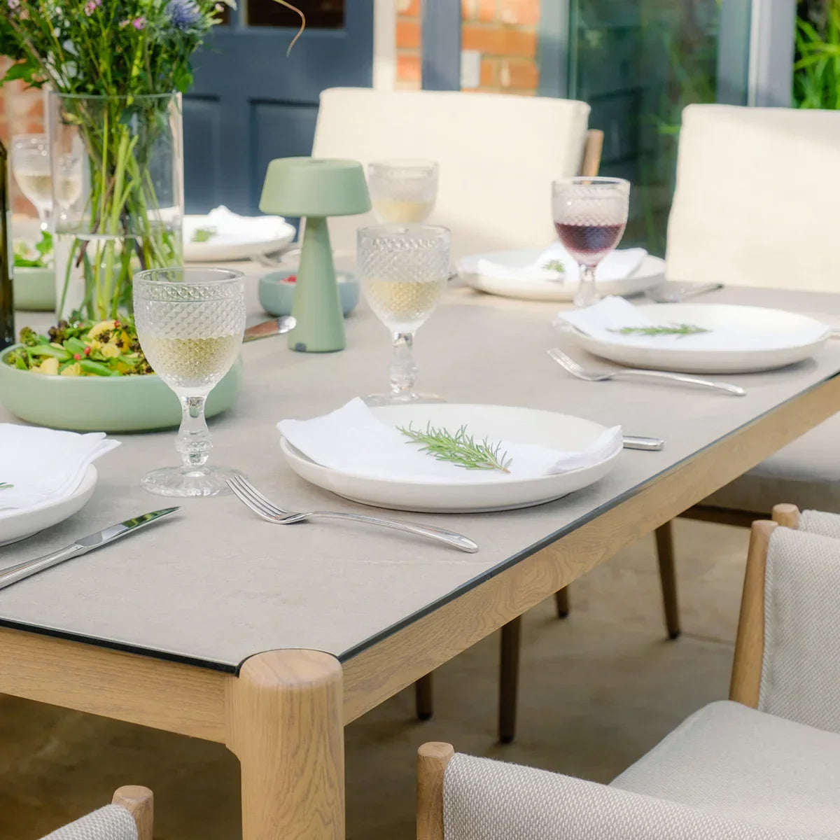 Modern dining table with light wood frame, beige top, and six chairs set for a meal