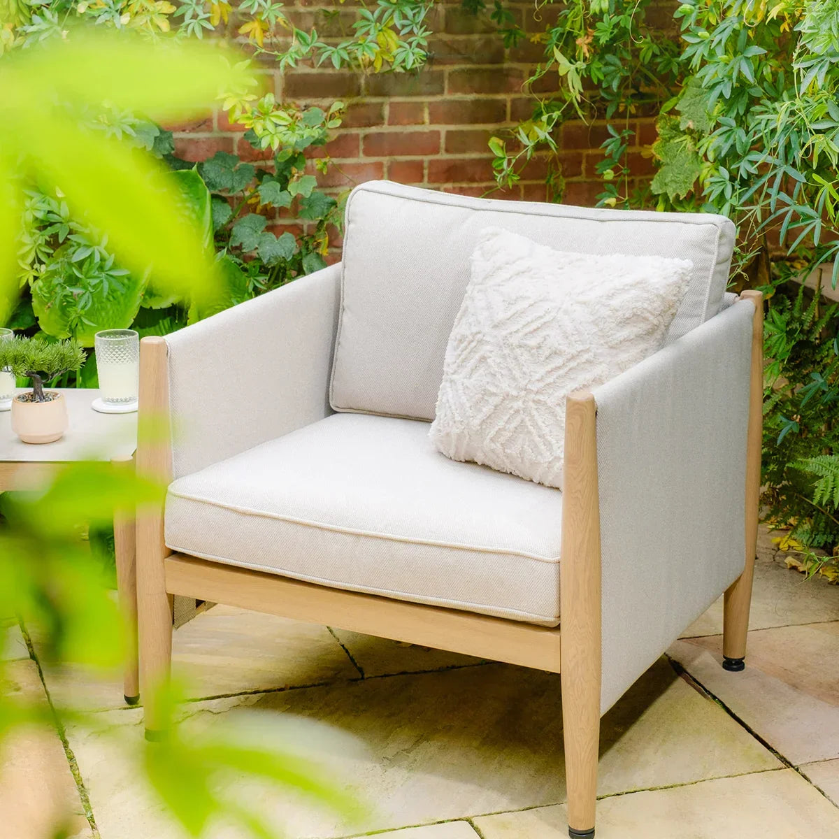 Outdoor lounge chair with light wood frame and cream cushions on a patio