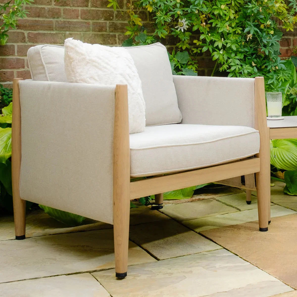 Beige outdoor armchair with wooden frame and plush cushion on stone patio