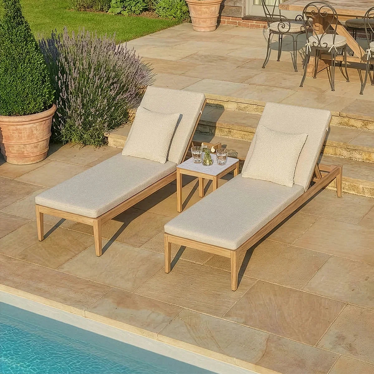 Pair of beige outdoor sun loungers with cushions beside a pool on stone patio