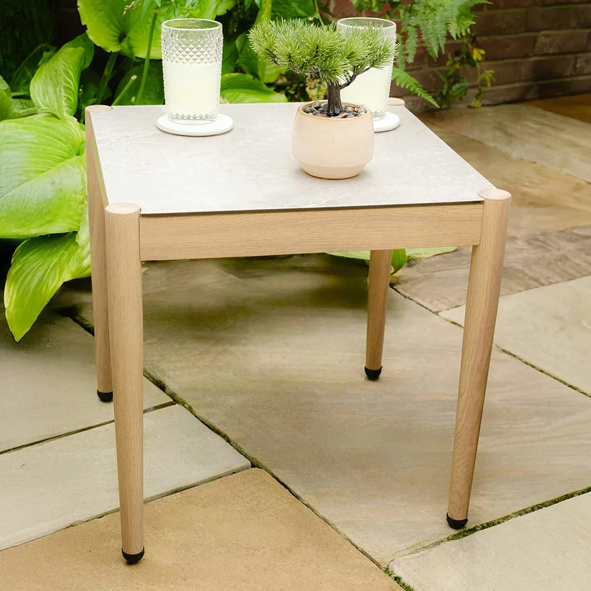Outdoor wooden side table with light stone top on patio, decorated with candles and plant