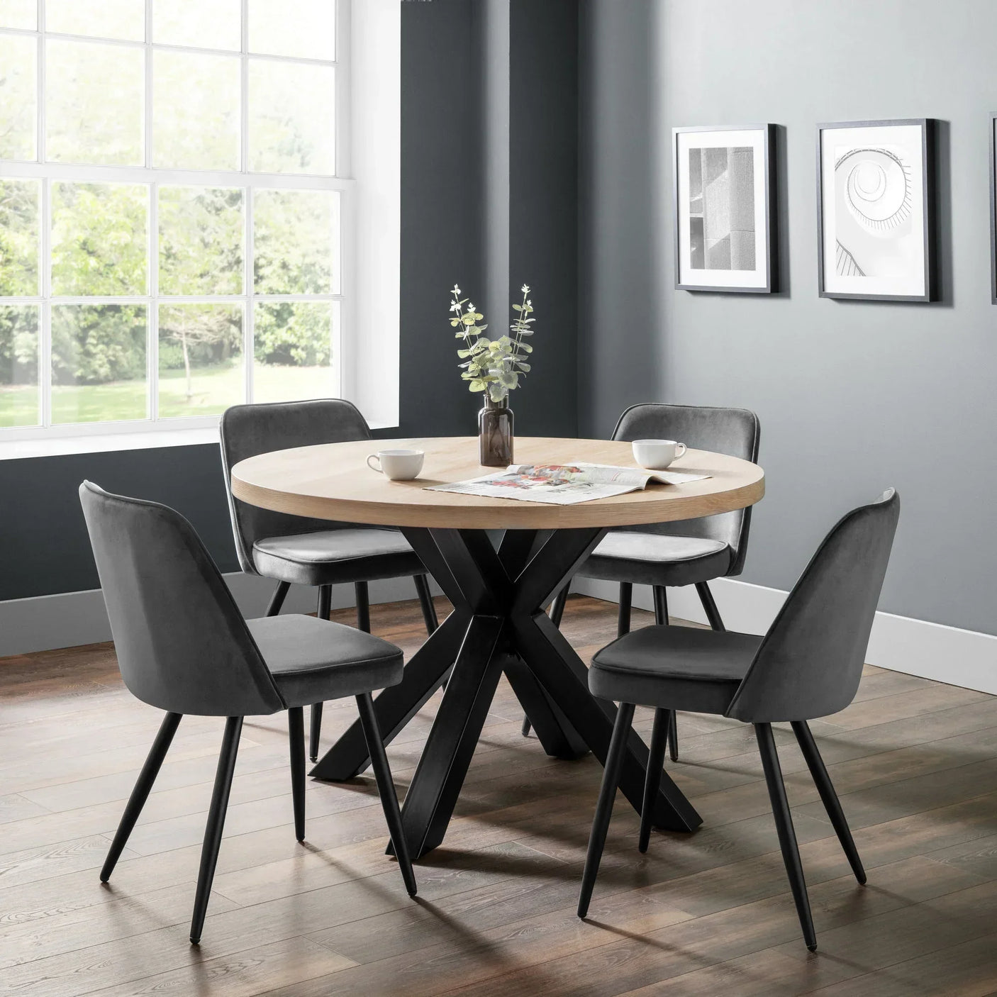Round wooden dining table with black legs and four grey velvet chairs in modern dining room