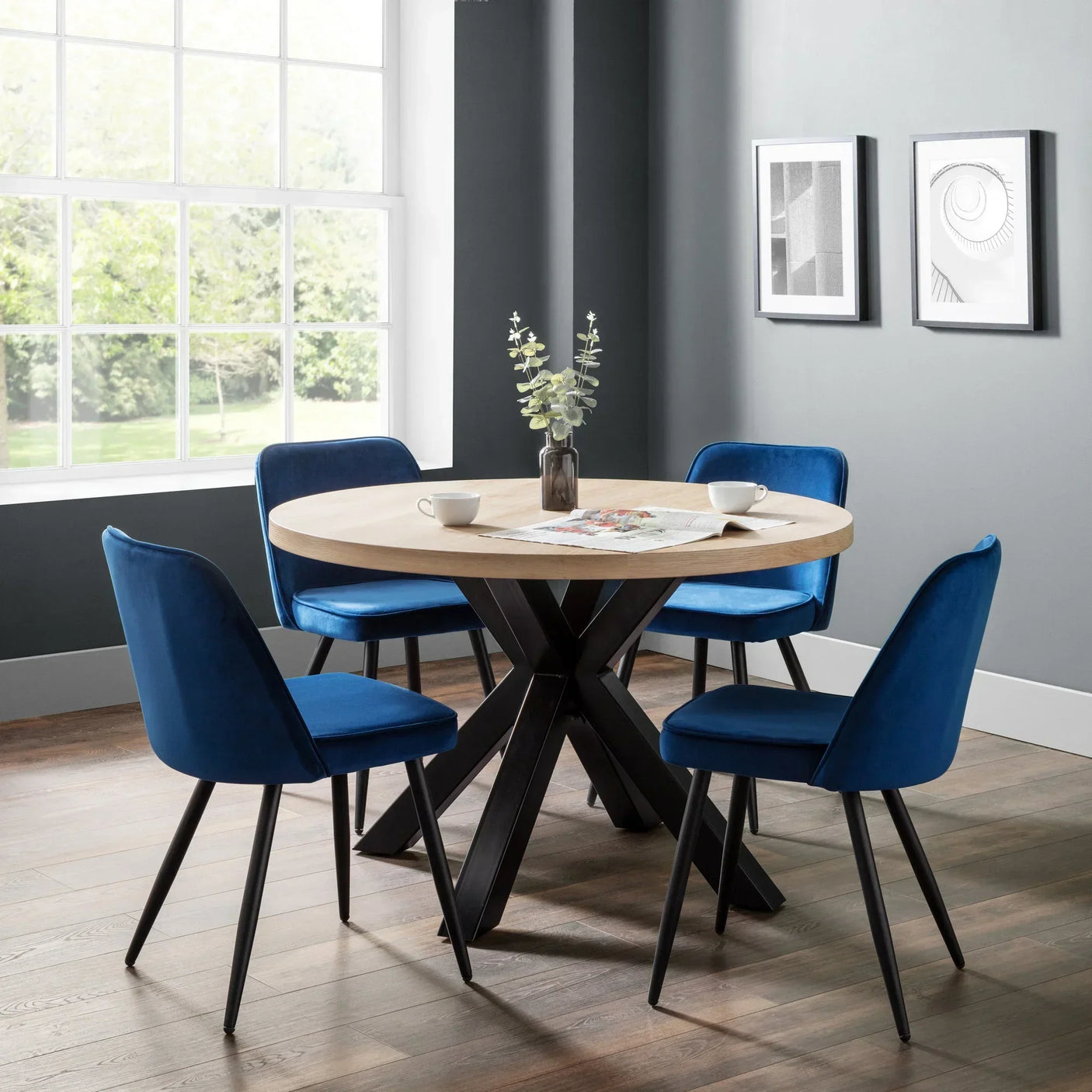 Round dining table with light wood top and four blue velvet chairs in modern dining room