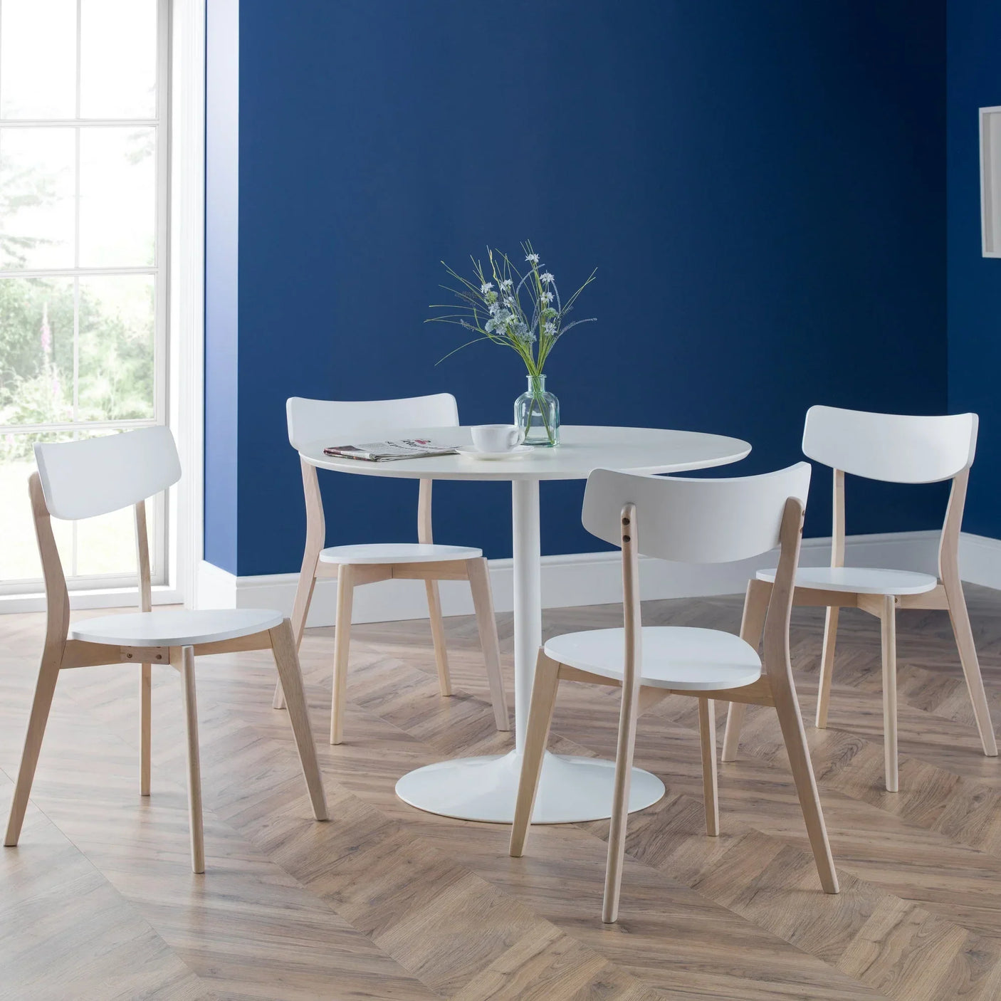 White round dining table with four white wooden chairs in modern room with blue wall