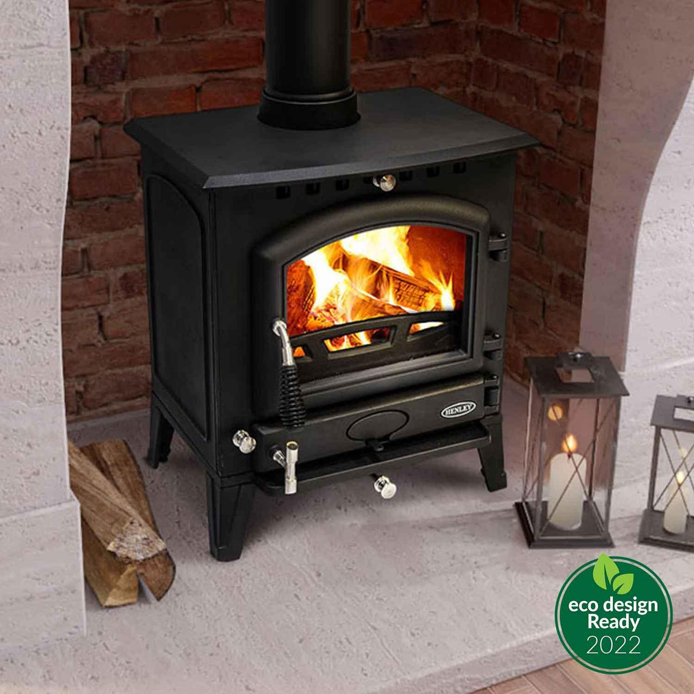Black Bracken Eco 7.9kW wood burning stove with fire, set on hearth beside lanterns