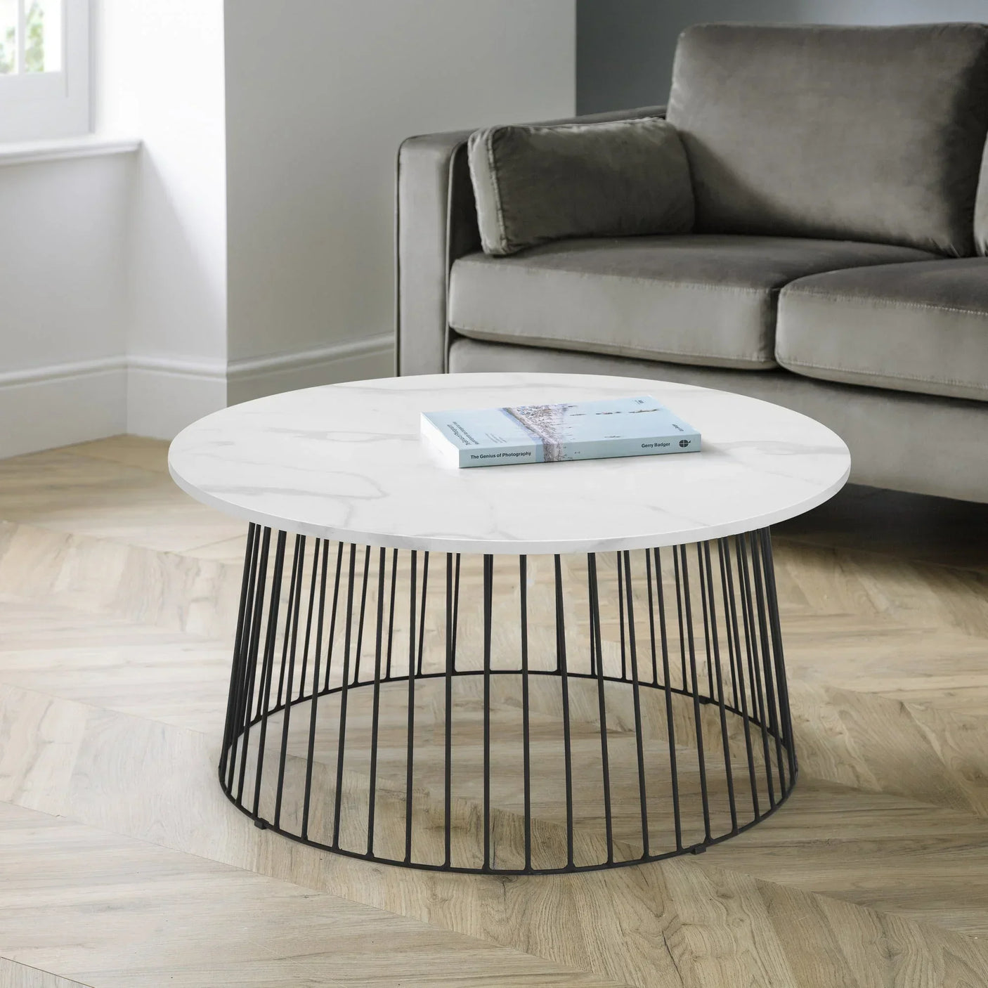 Round marble coffee table with black metal base in modern living room next to grey sofa