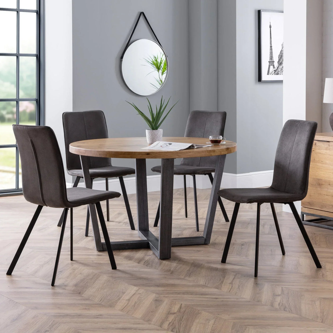 Round oak dining table with four grey fabric chairs in modern dining room setting