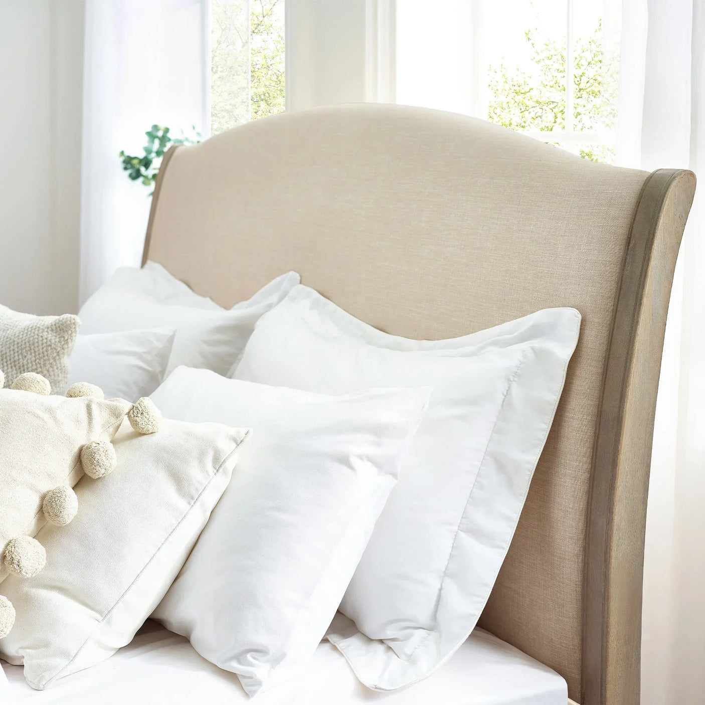 Cream upholstered double bed headboard with white pillows in bright room