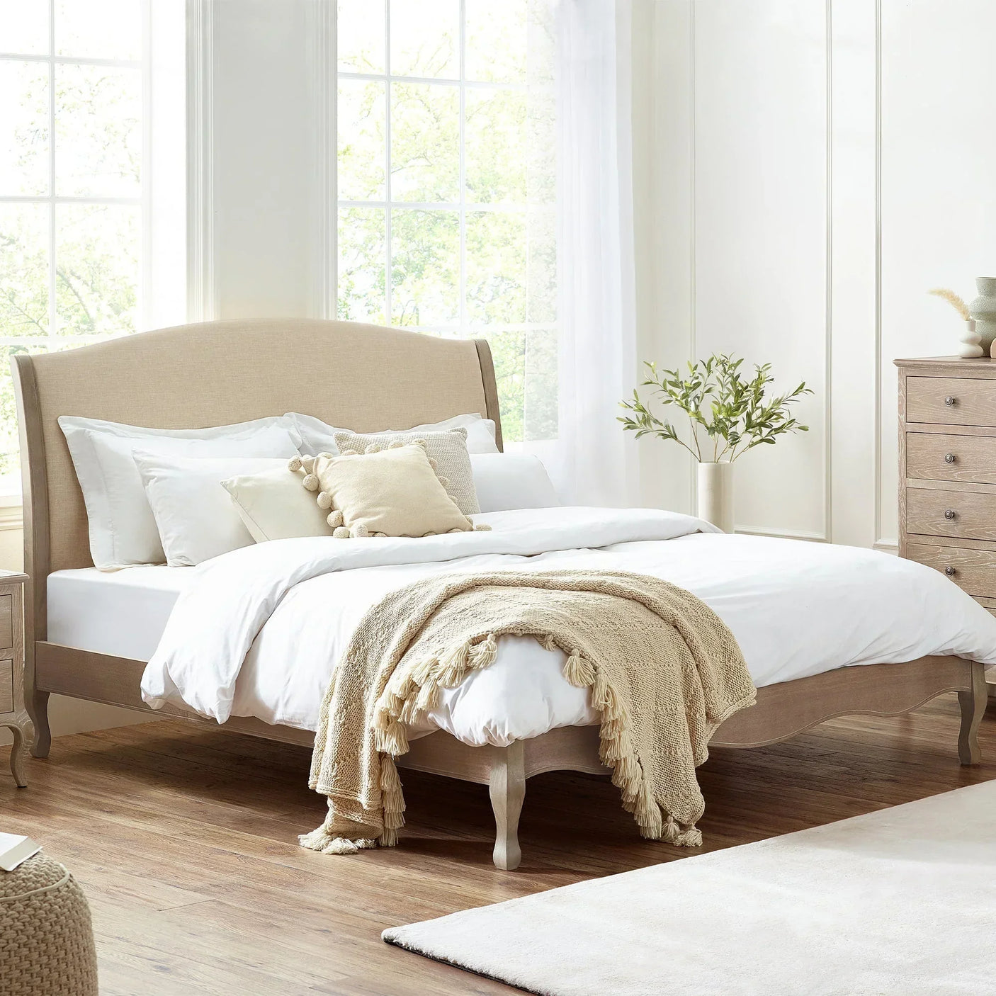 Beige double bed with upholstered headboard, white bedding and throw in bright bedroom