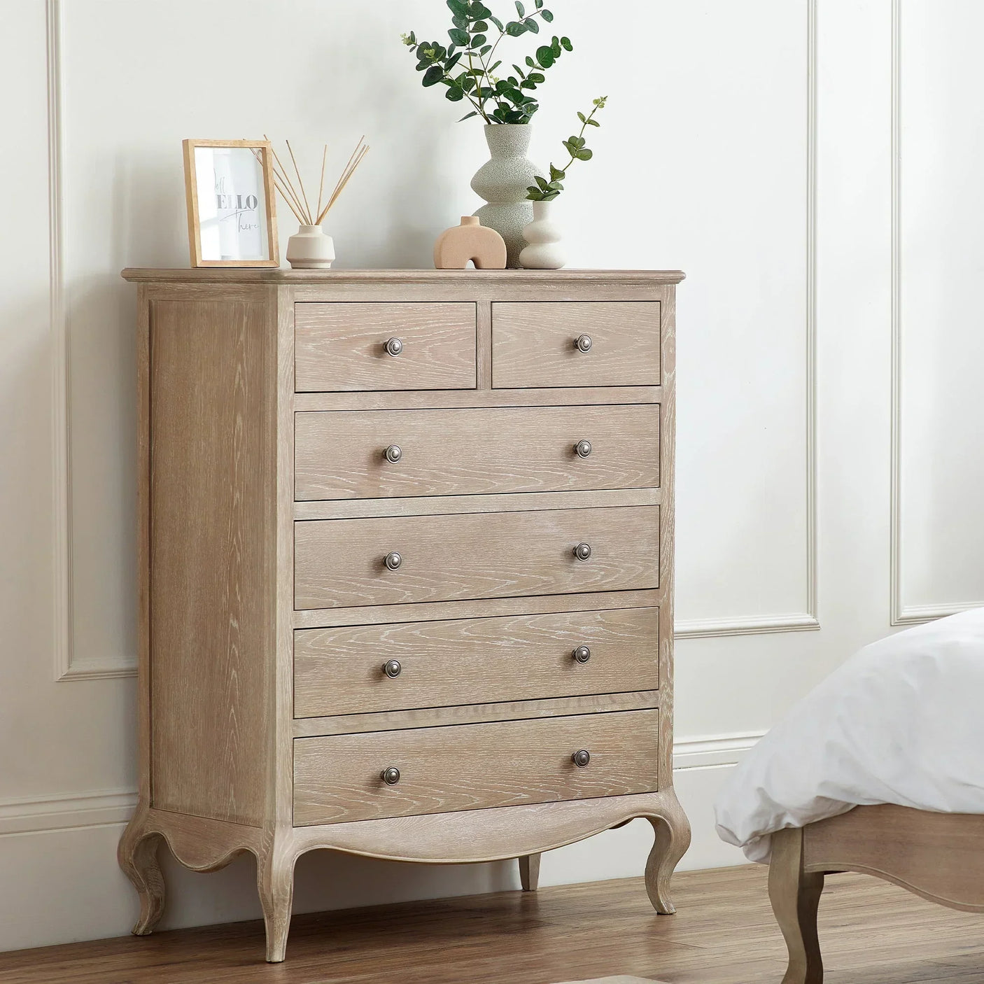 Oak chest of drawers with metal knobs beside bed, decorated with vases and framed photo