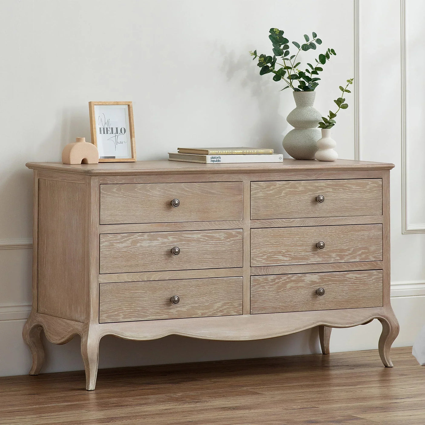 Oak six drawer wide chest with curved legs, styled with books and vases in a modern room