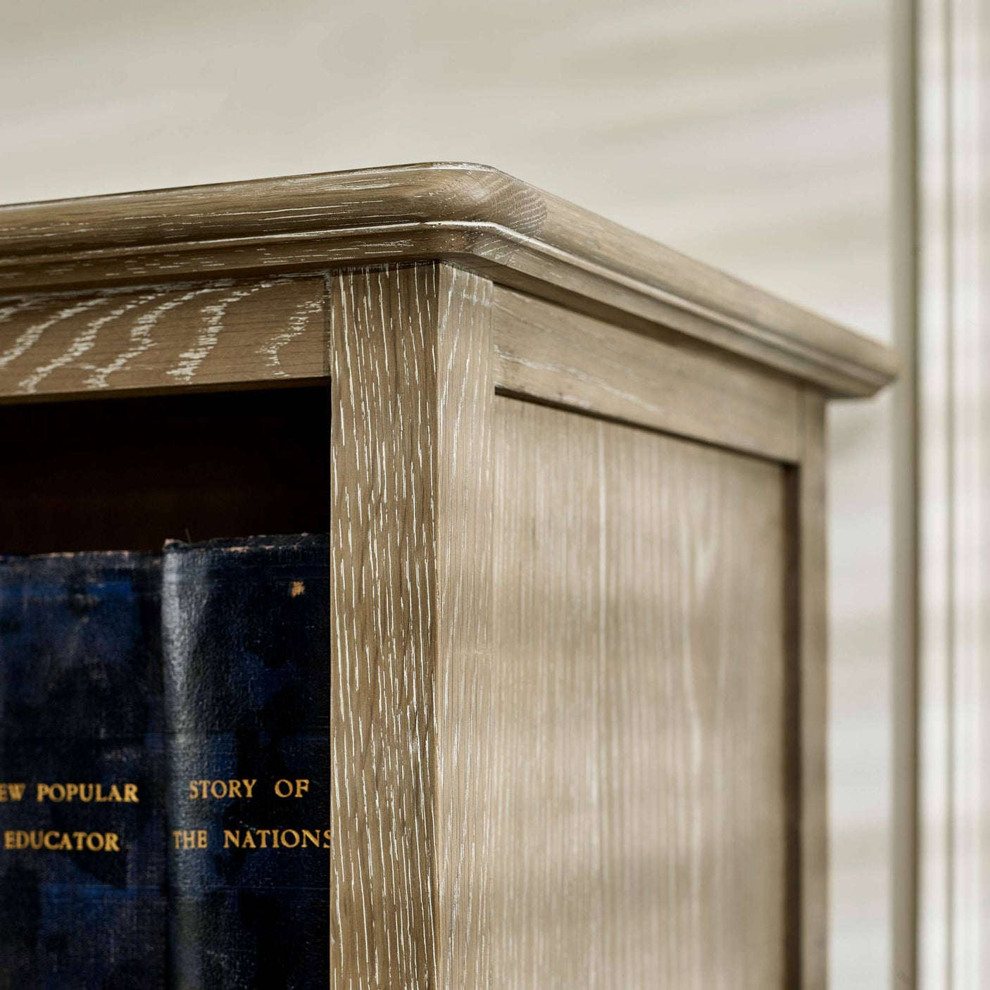 The Camille French Style Tall Bookcase features a limed oak finish with a textured surface, showcasing its elegant design and sturdy construction, perfect for displaying books and decorative items in a stylish living space