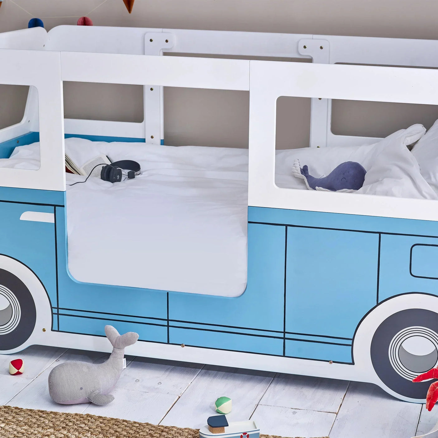 Blue campervan kids bed with white bedding, soft toy whale and playful decor
